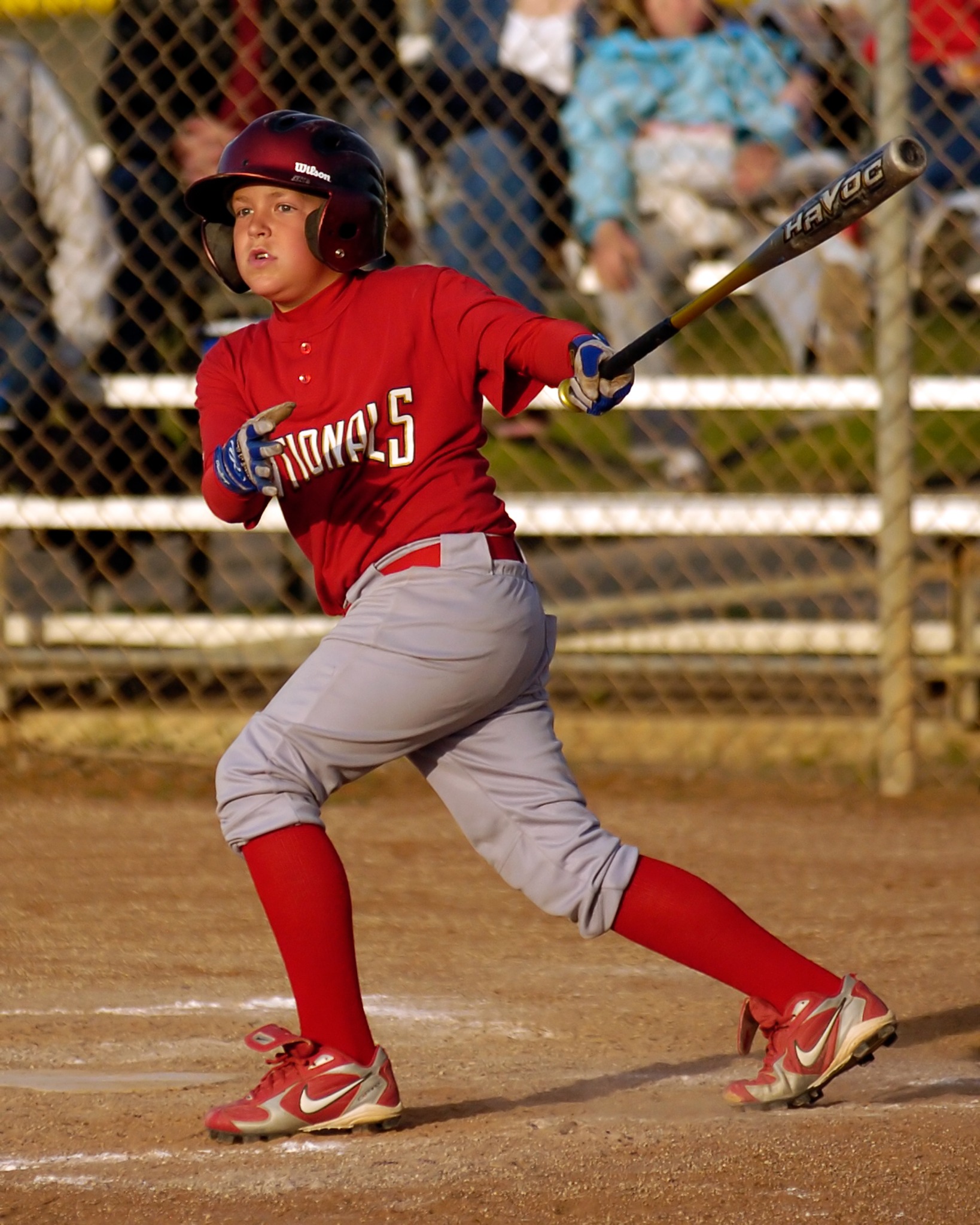 Youth baseball player in red uniform finishing a swing at home plate