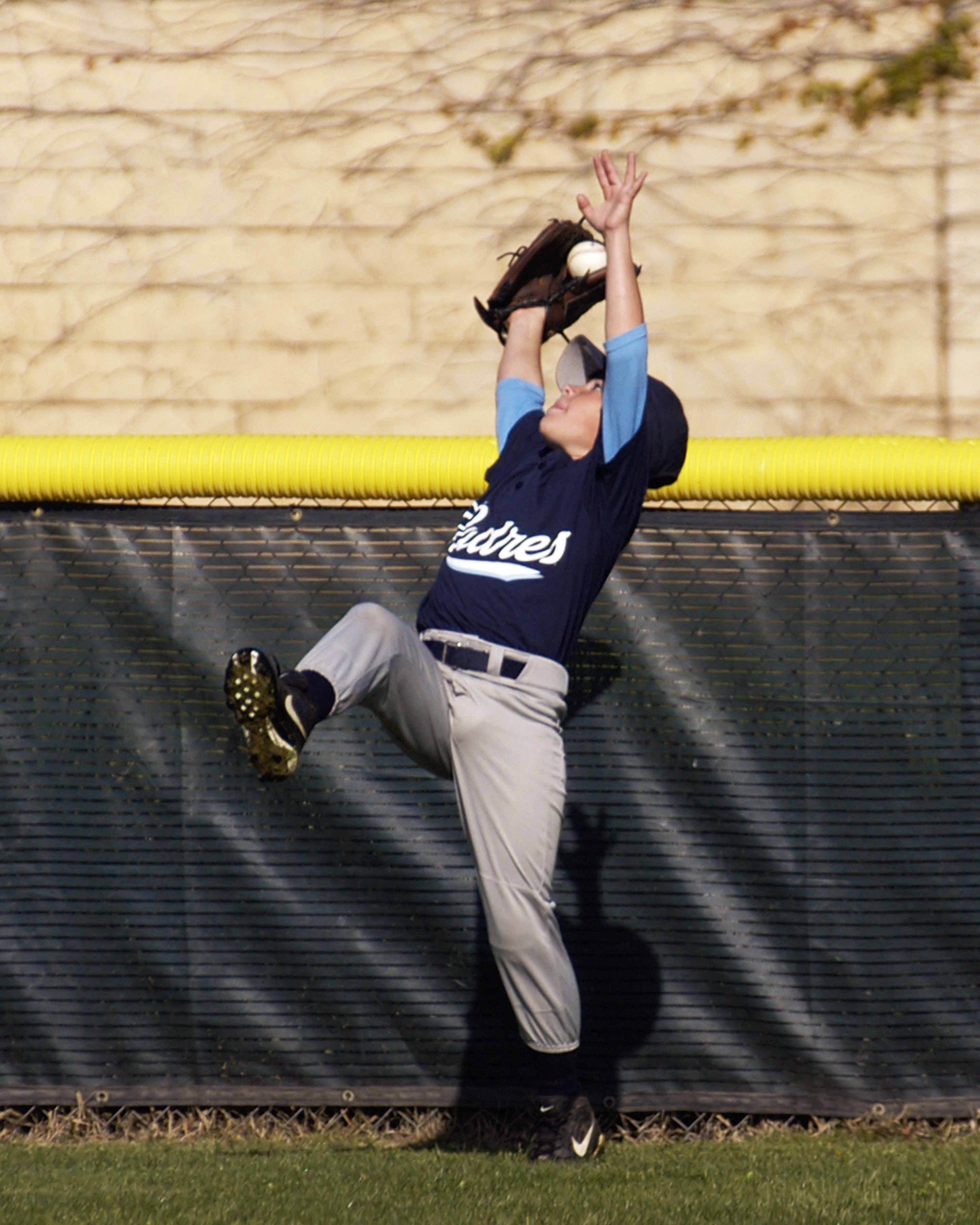 Youth baseball outfielder reaching high for a catch near the fence